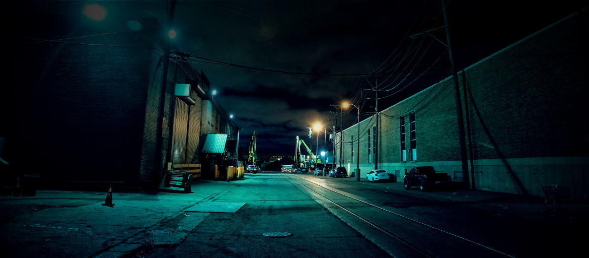 a dark side street leading to a line of industrial warehouses